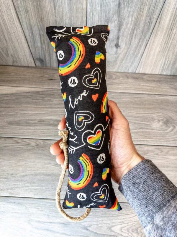 A hand holding a catnip kicker made from a black fabric that has a pattern of rainbows and the word "love" on it. 
