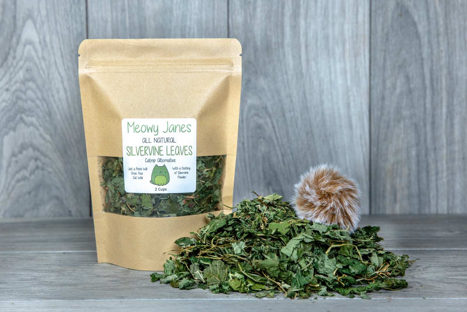 A bag of silvervine leaves with a pile of silvervine leaves next to it with a fuzzy ball toy.