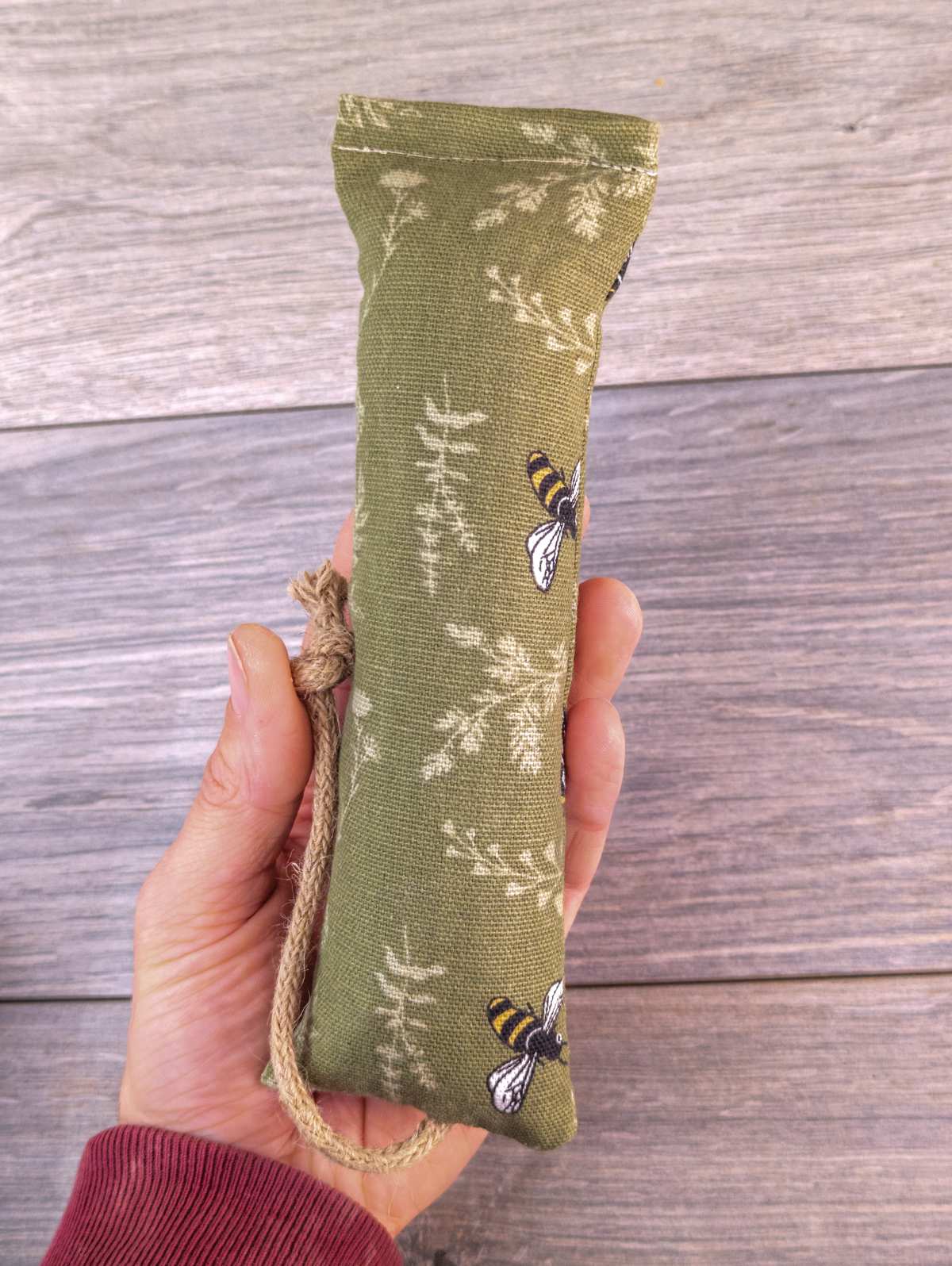 A hand holding a catnip kicker made out of a green bee themed fabric.