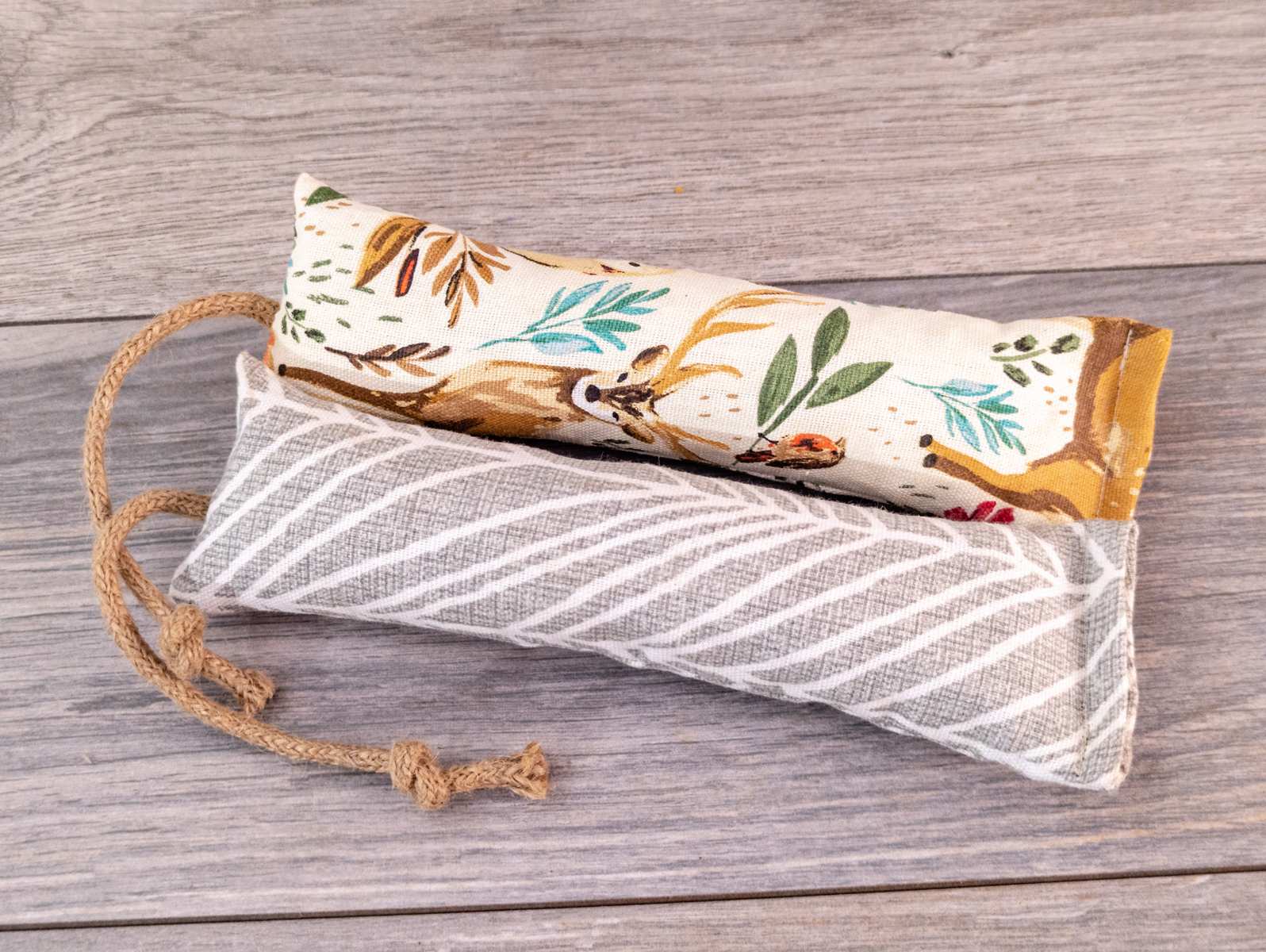Two catnip kicker cat toys made out of a grey striped fabric and white woodland themed fabric.
