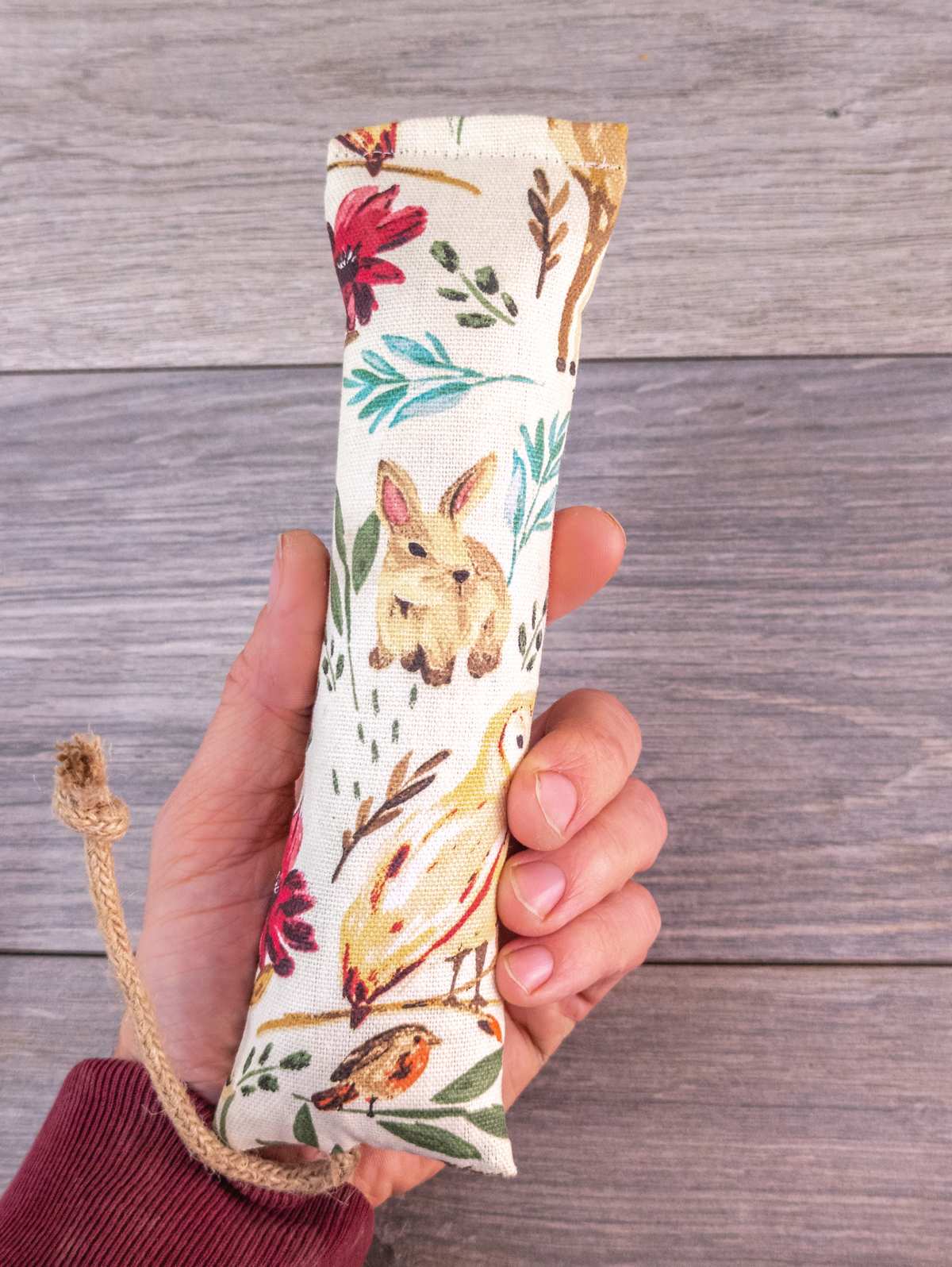 A hand holding a catnip kicker made white woodland themed fabric.