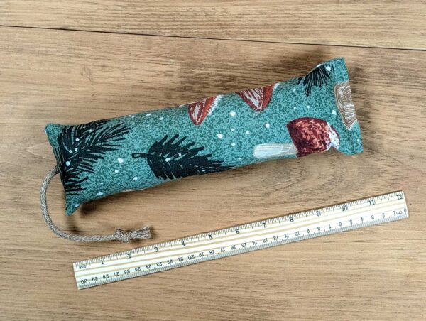 A catnip filled kicker with green fabric, pine leaves, and  mushrooms on it.