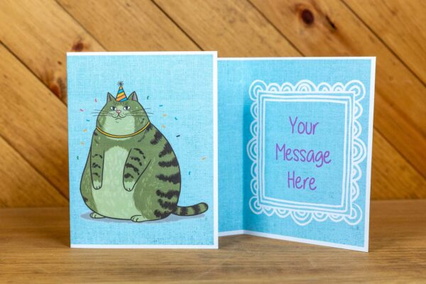 A greeting card with a fat green cat wearing a small birthday hat on front